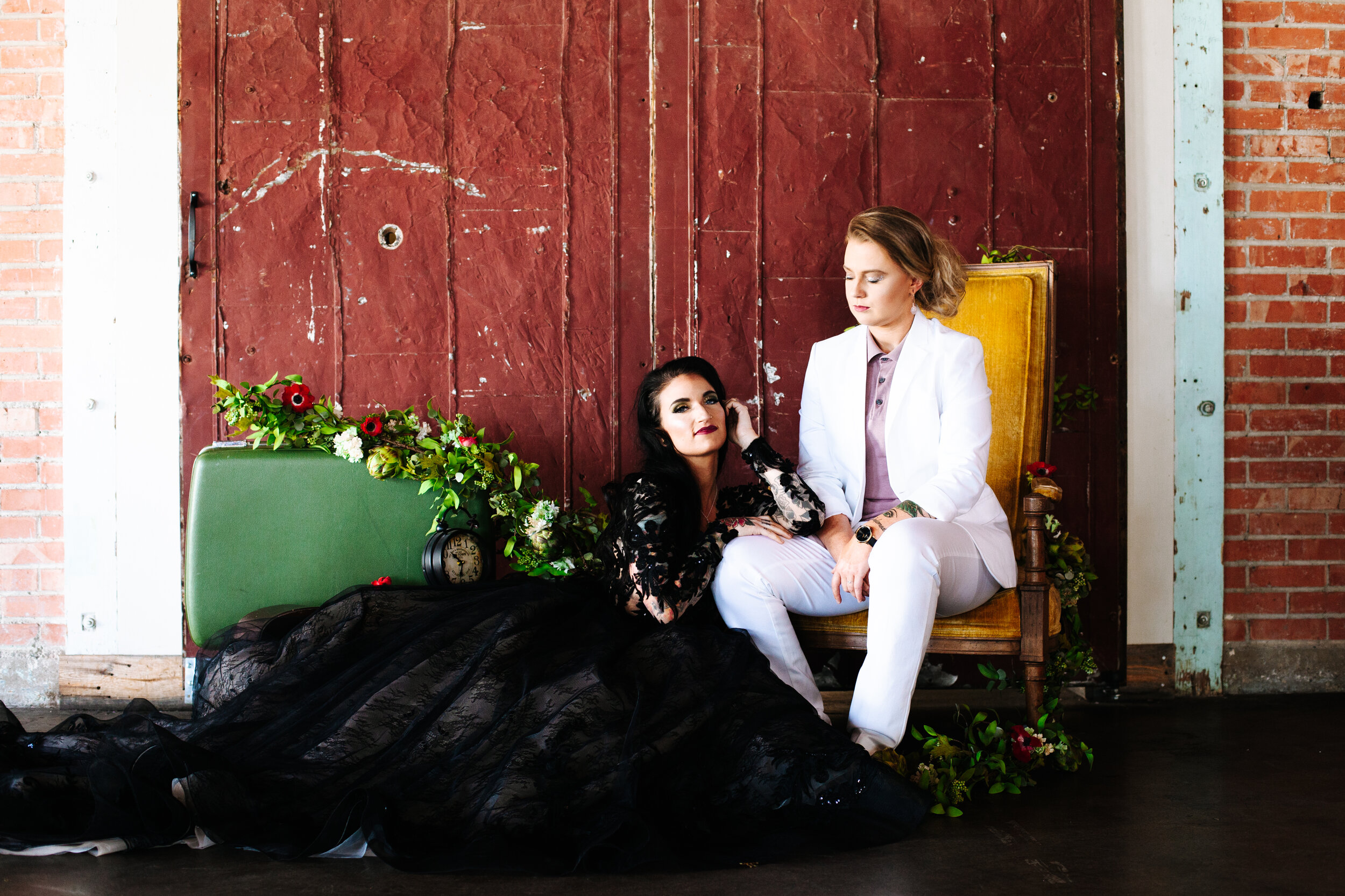 Lesbian couple sitting together at their wedding in Utah. One woman is wearing a black Sottero and Midgely ball gown wedding dress and the other woman wears a white suit with a mauve polo underneath. 