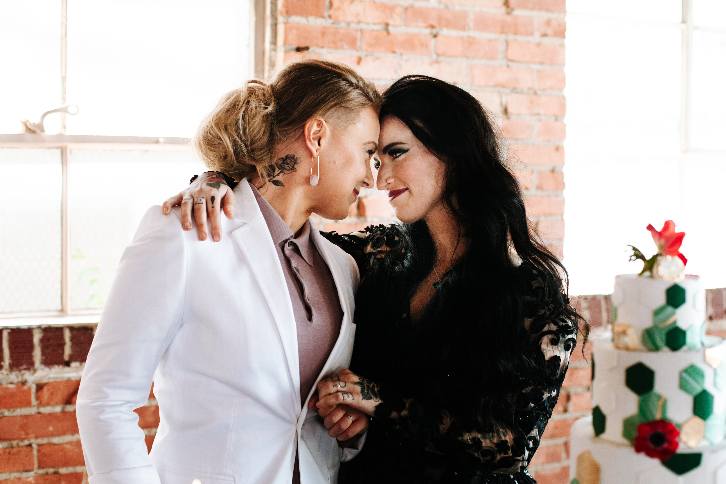 Lesbian brides at their wedding looking at each other lovingly, their foreheads are touching. 
