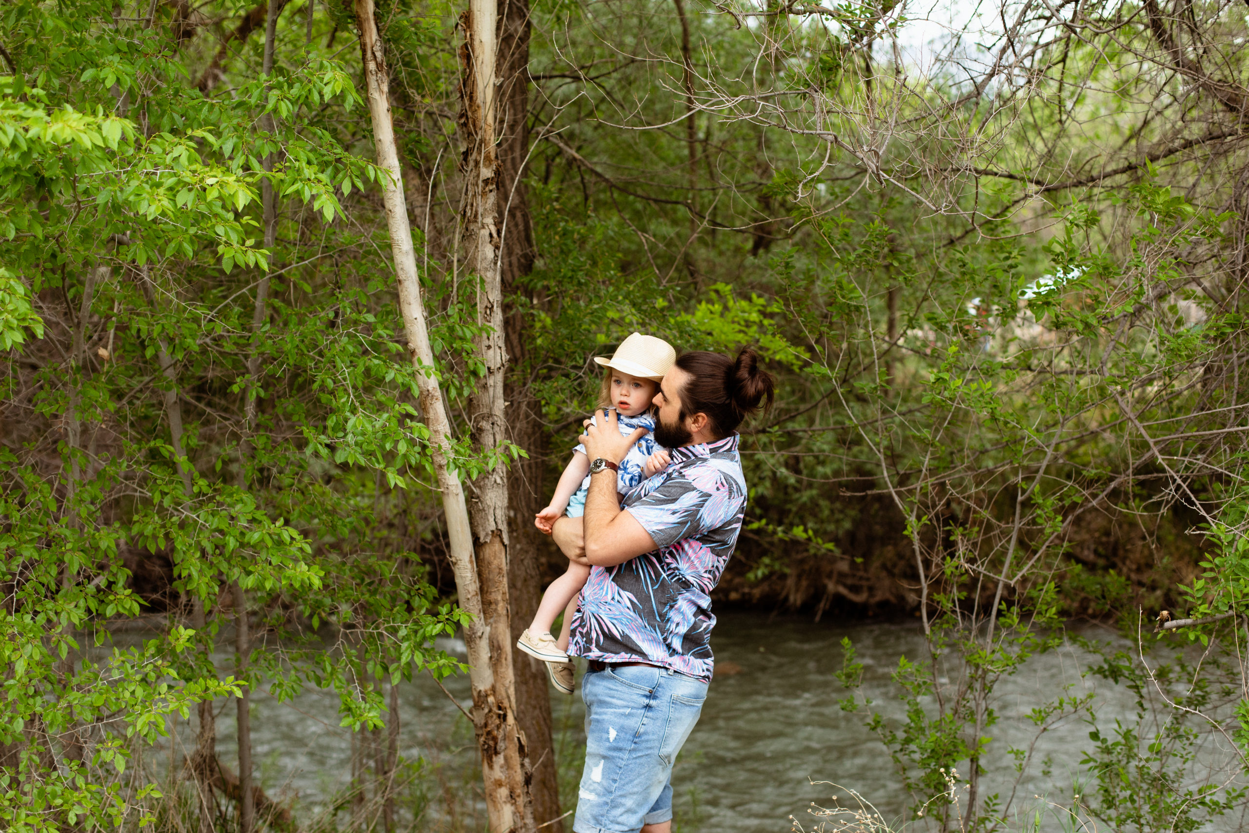 A father is holding his child, a river is running behind them at Wheeler Farm.