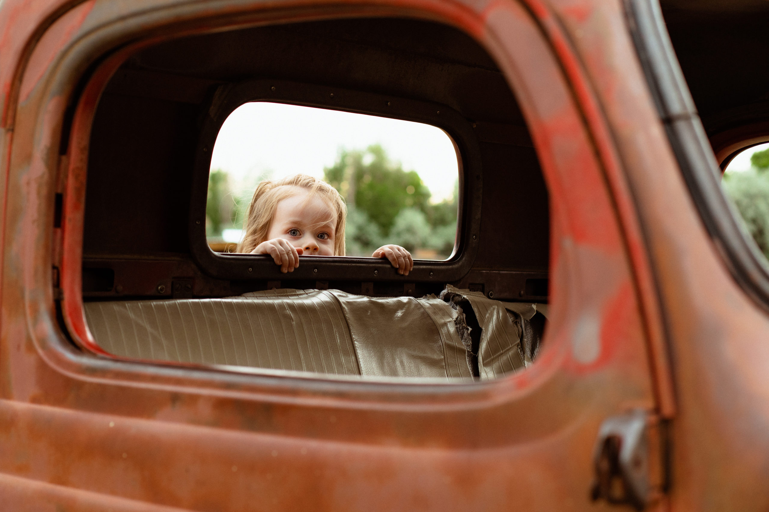Toddler peeking through a vintage pickup truck window at Wheeler Farm.